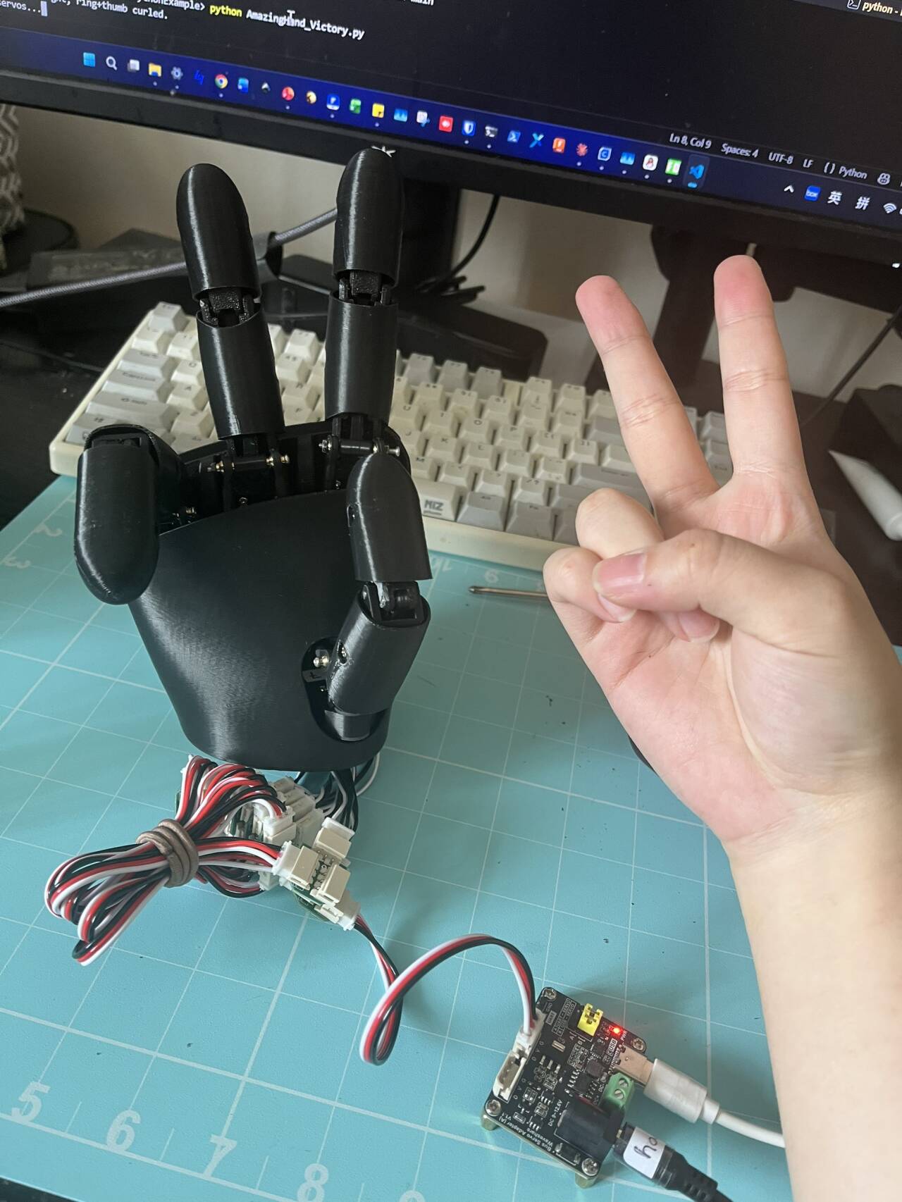3D-printed AmazingHand dexterous hand making a victory sign next to a human hand